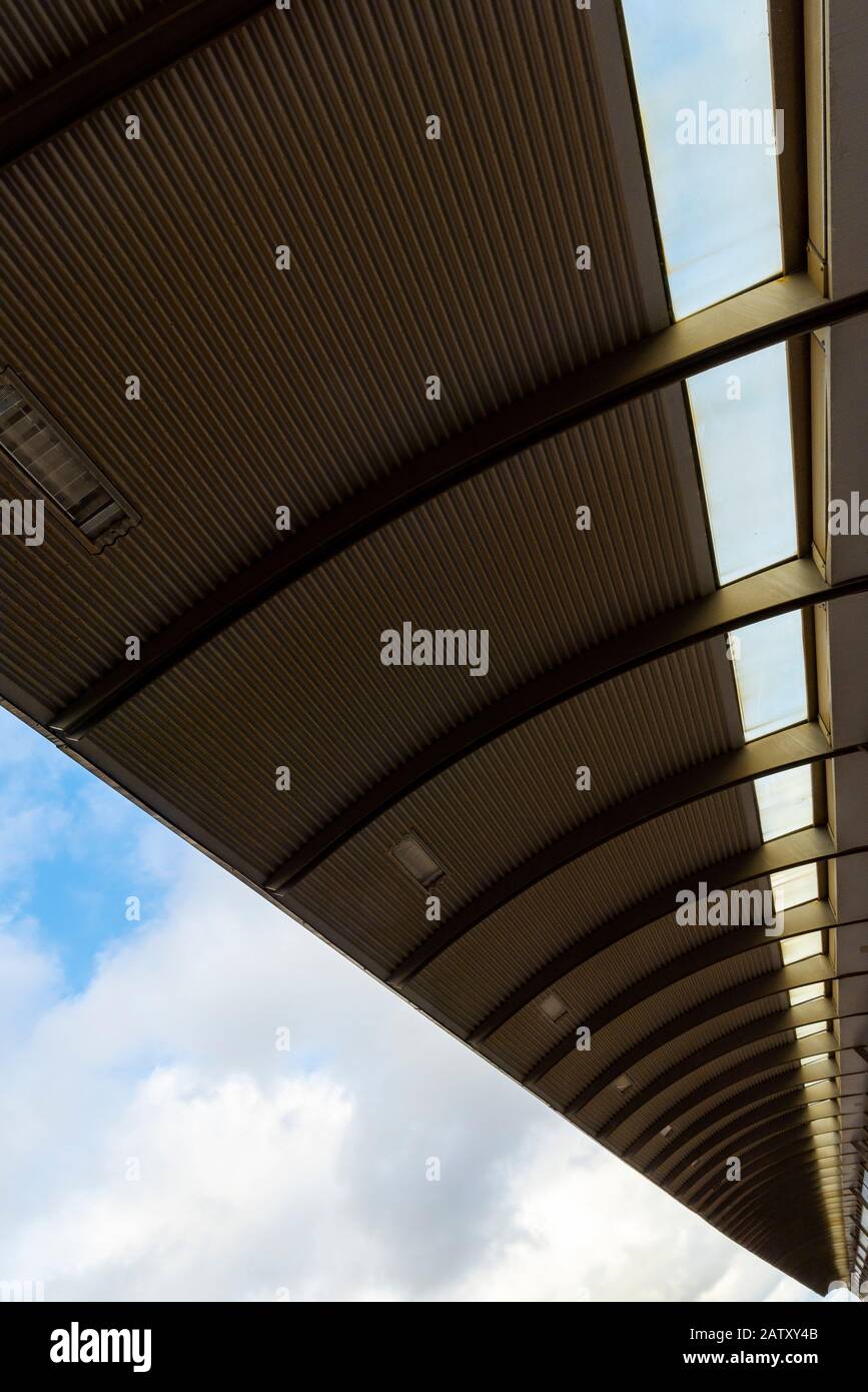 Vista dal basso di un tetto in metallo da una piattaforma della stazione ferroviaria. Costruzione di tetti in acciaio sotto il cielo blu Foto Stock