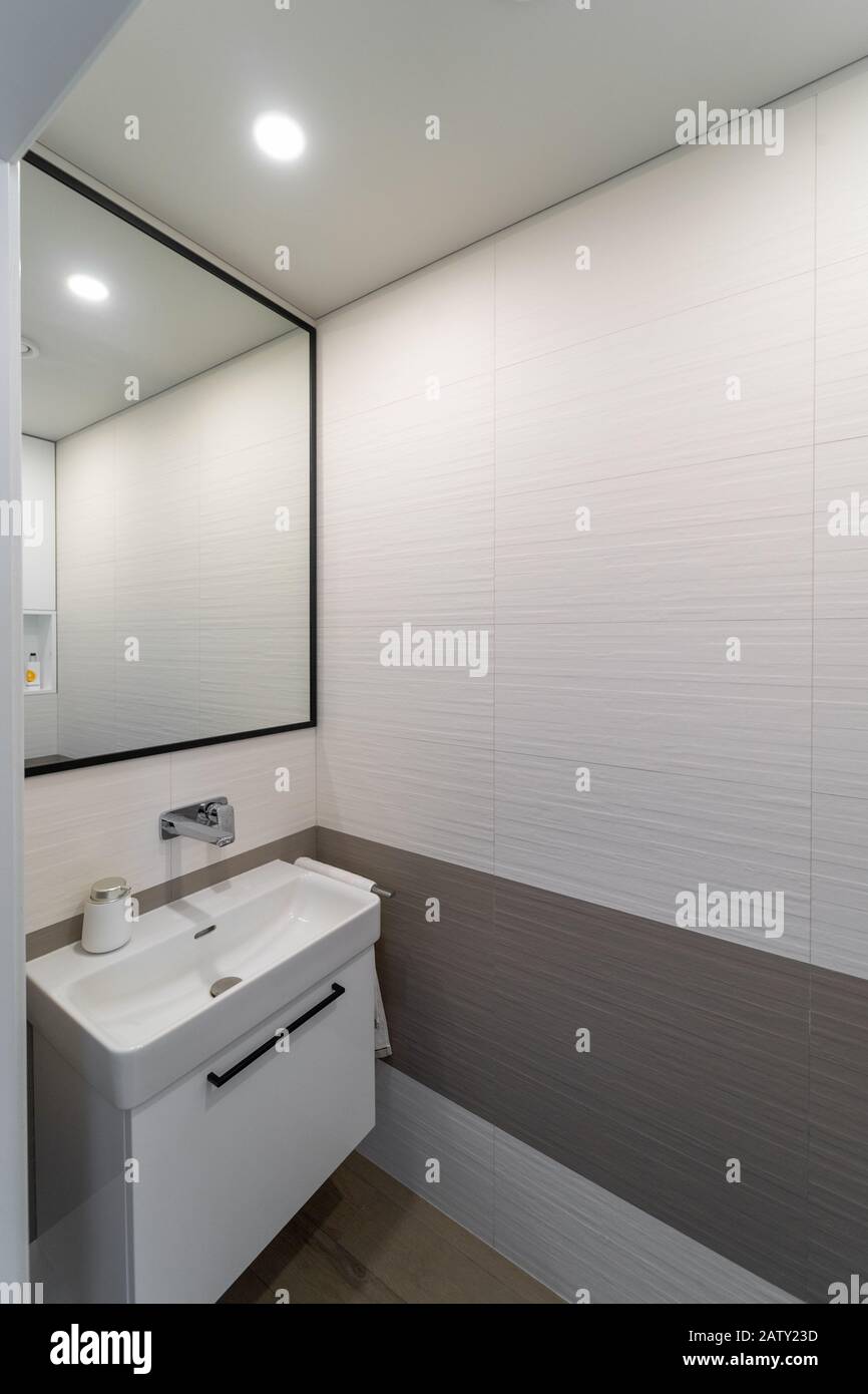 Moderni e nuovi interni in toilet di colore chiaro, con pareti beige e marrone e pavimento piastrellato. Lavandino bianco sull'armadio. Accanto ad esso - un asciugamano sospeso, sopra di me Foto Stock