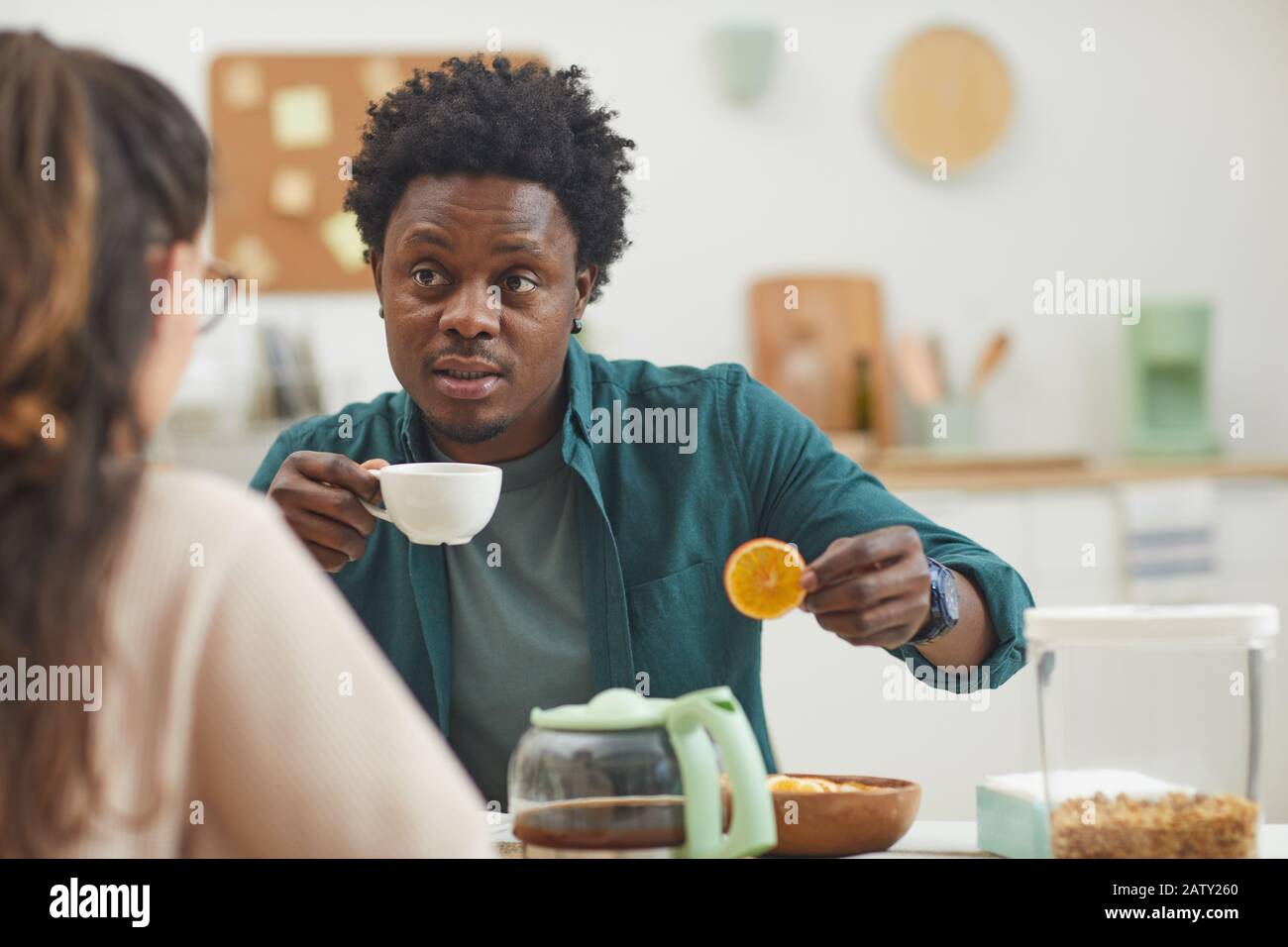 Giovane africano bere caffè con biscotti e parlare con la sua ragazza in cucina a casa Foto Stock