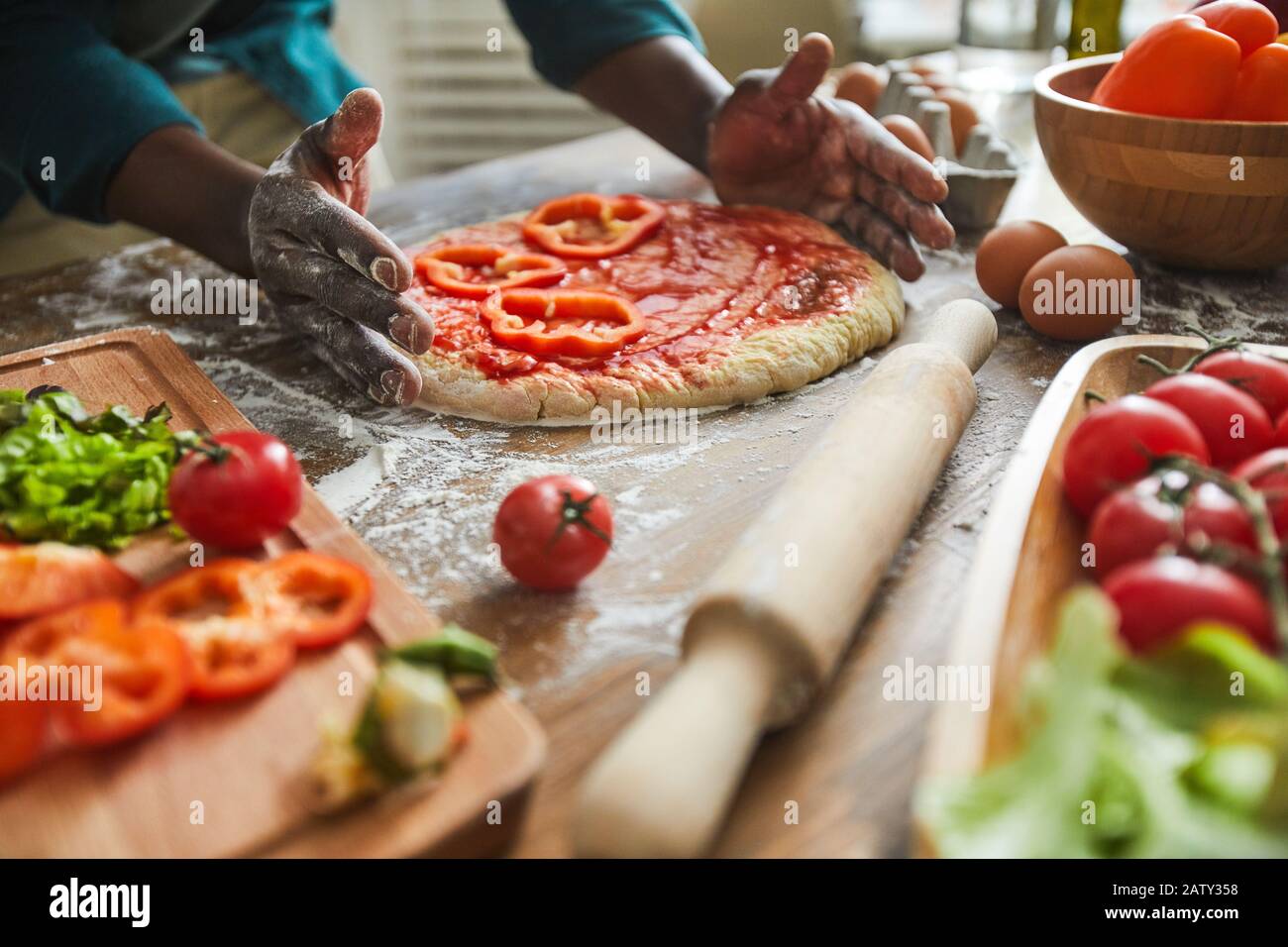 Primo piano di uomo africano che fa la pizza con verdure al tavolo di legno in cucina Foto Stock