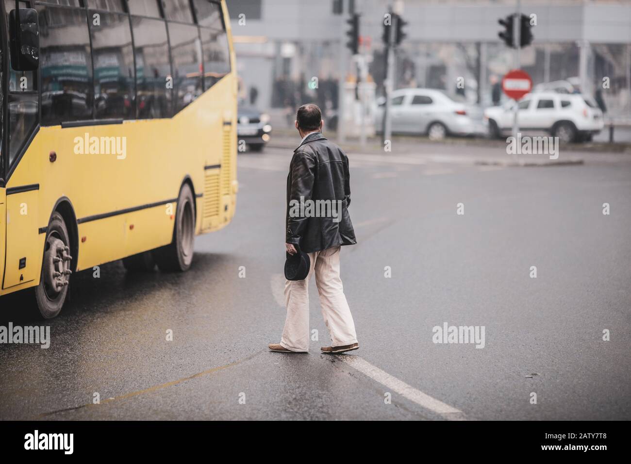 Uomo anziano che attraversa illegalmente la strada nel mezzo di un incrocio. Foto Stock