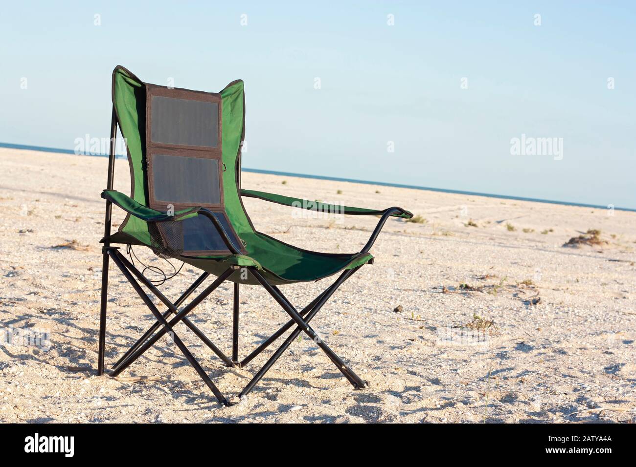 Un pannello solare pieghevole portatile si aggancia a una sedia da viaggio. Campeggio turistico in estate sulla riva del mare. Foto Stock