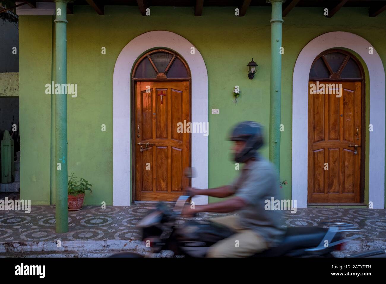 Fontainhas, Panaji, Goa, India - 27 febbraio 2018: Motociclista irriconoscibile che passa da una casa verde nel famoso quartiere di Fontainhas Foto Stock