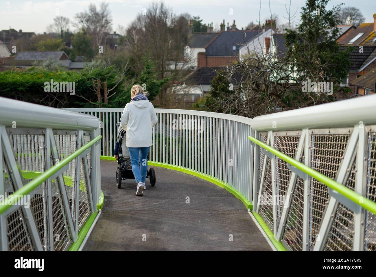 Una giovane donna che spinge un carrozzone o passeggino su un moderno ponte a spirale in metallo Foto Stock