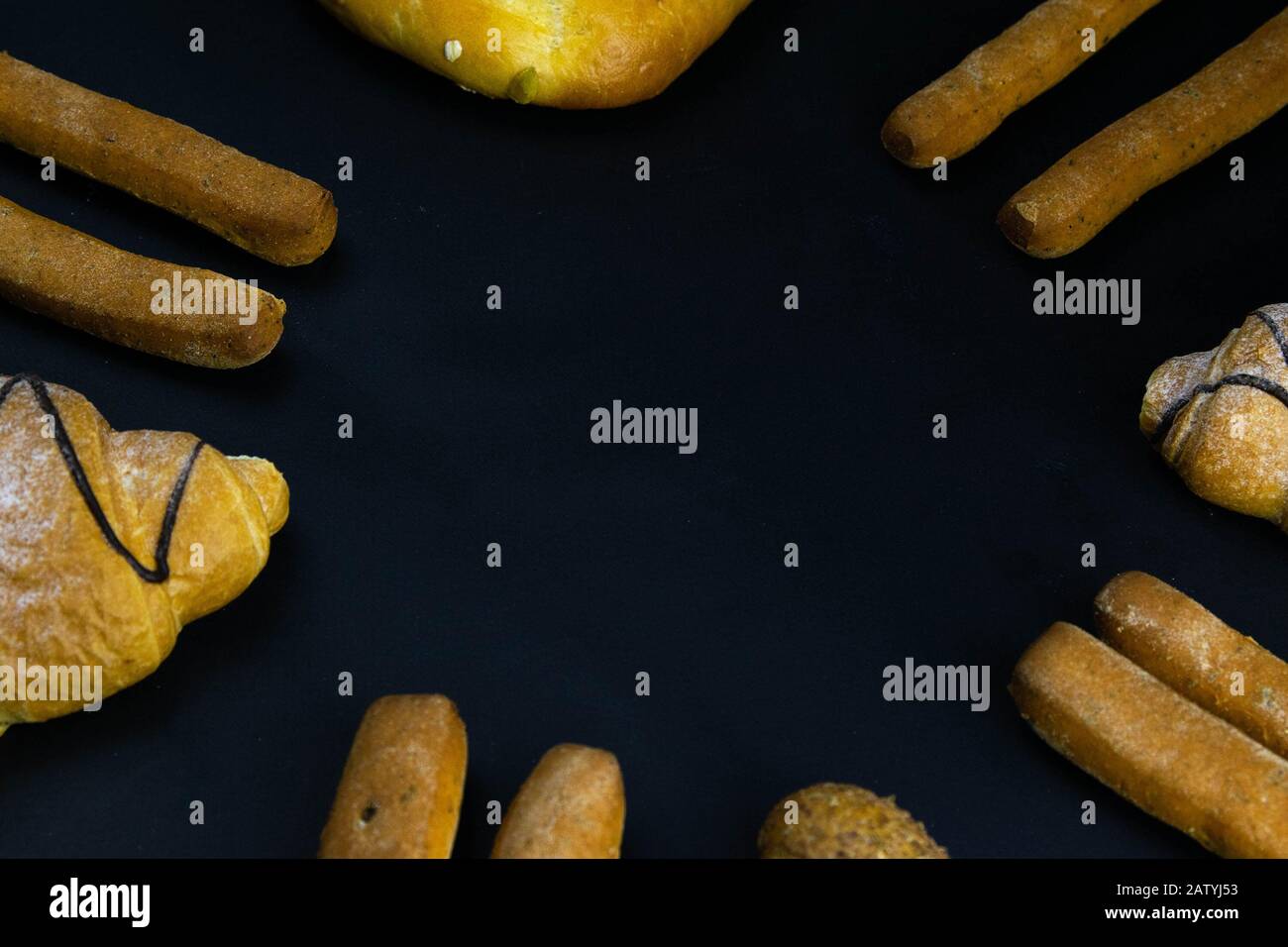 Diversi tipi di pane fresco con grano su sfondo rustico nero. Il pane si erge intorno Foto Stock