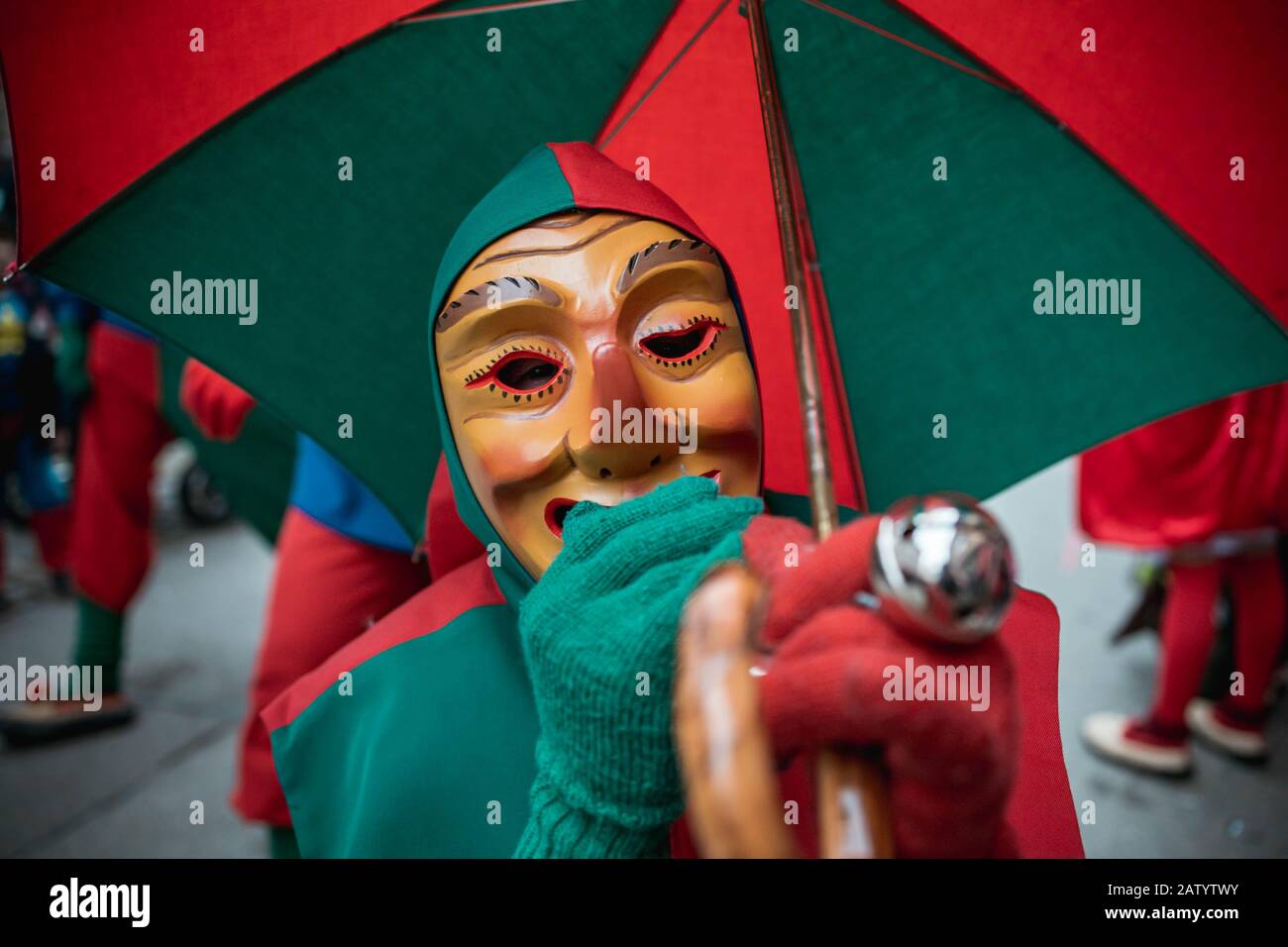 Oberwindemer Spitzbue - sciocco di Carnevale in accappatoio rosso-verde e ombrello durante la sfilata di Carnevale a Staufen, Germania meridionale. Foto Stock