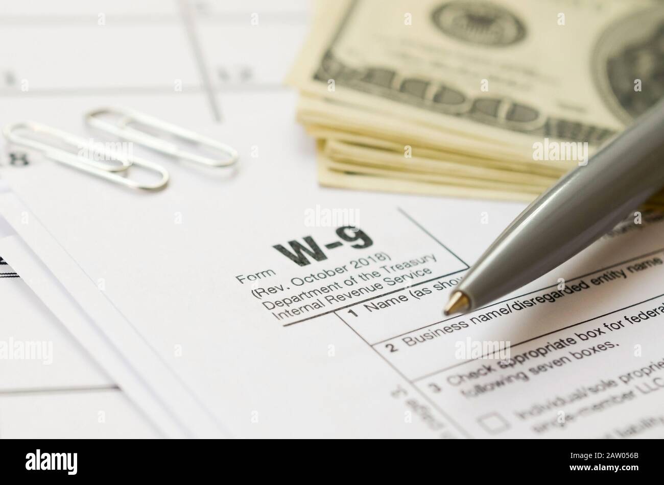 IRS Form W-9 richiesta per il contribuente un numero di identificazione e certificazione giace vuoto con penna e molte centinaia di fatture del dollaro nella pagina calendario. Imposta peri Foto Stock