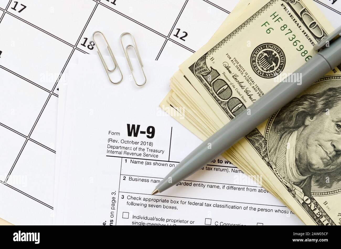 IRS Form W-9 richiesta per il contribuente un numero di identificazione e certificazione giace vuoto con penna e molte centinaia di fatture del dollaro nella pagina calendario. Imposta peri Foto Stock