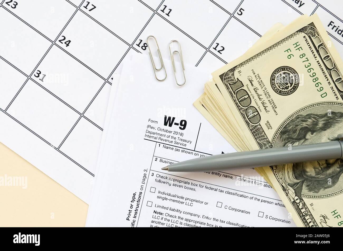 IRS Form W-9 richiesta per il contribuente un numero di identificazione e certificazione giace vuoto con penna e molte centinaia di fatture del dollaro nella pagina calendario. Imposta peri Foto Stock