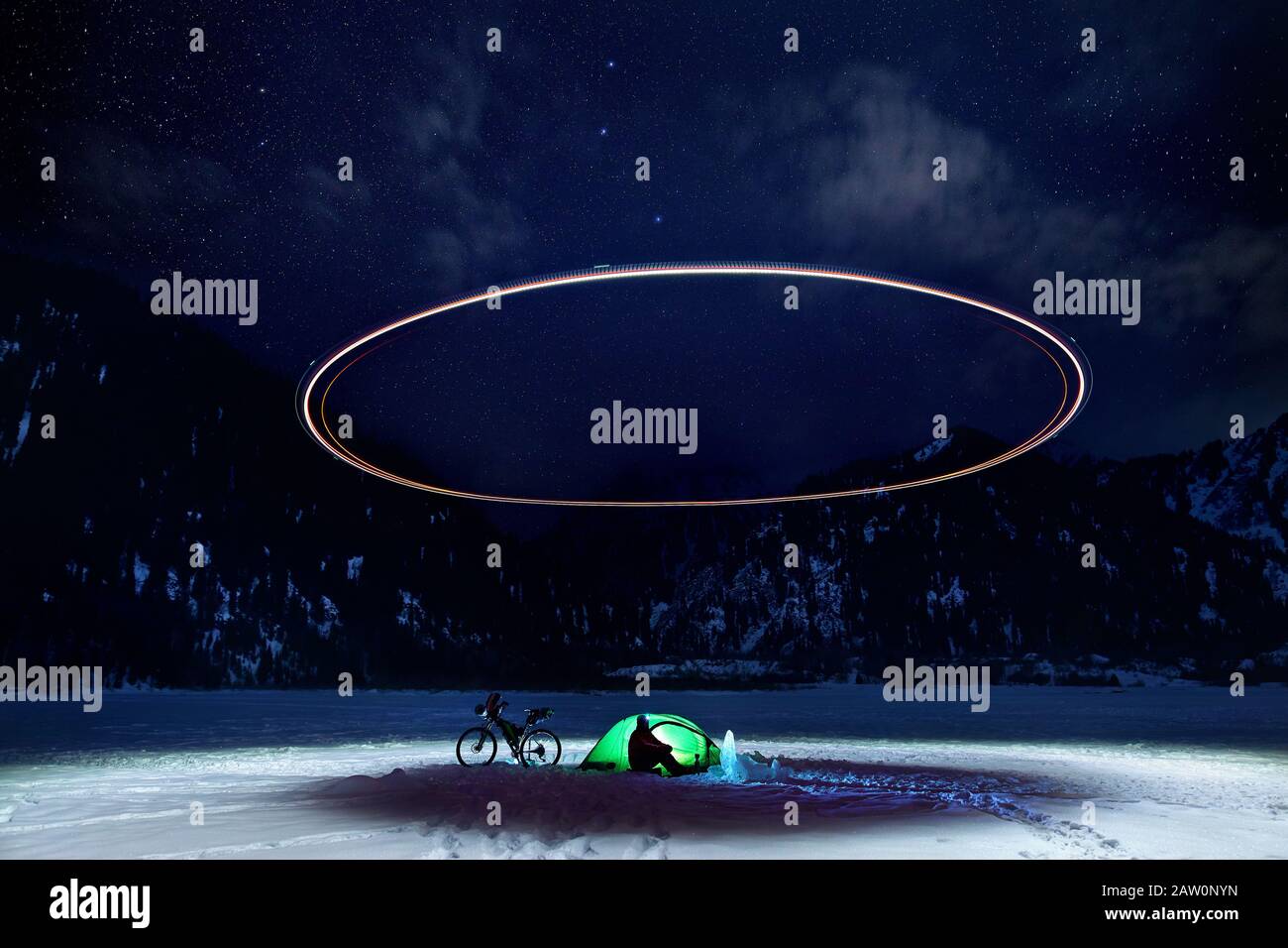 Uomo in campo con bicicletta e tenda verde al lago ghiacciato in montagna. Drone che illumina il cerchio di luce sopra il campo con starry notte cielo backgroun Foto Stock