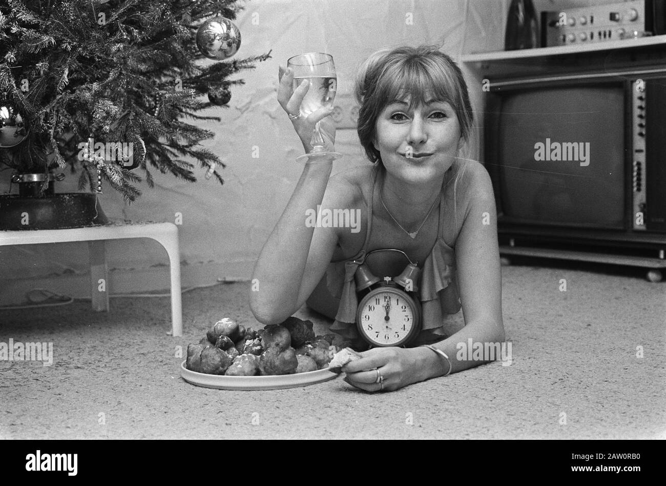 Capodanno; giovane donna con ciambelle, sveglia e champagne Data: 28 dicembre 1975 Parole Chiave: Champagne, cambi di anno, ciambelle Foto Stock