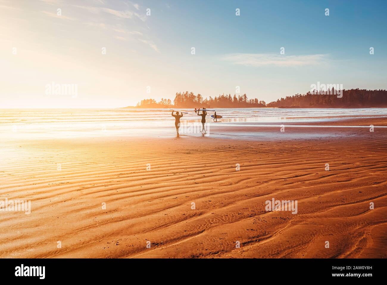 Surfisti sulla spiaggia camminando verso l'oceano. Ora del tramonto, ora d'oro. Giornata di sole sulla costa dell'oceano. Tofino, British Columbia, Canada Foto Stock