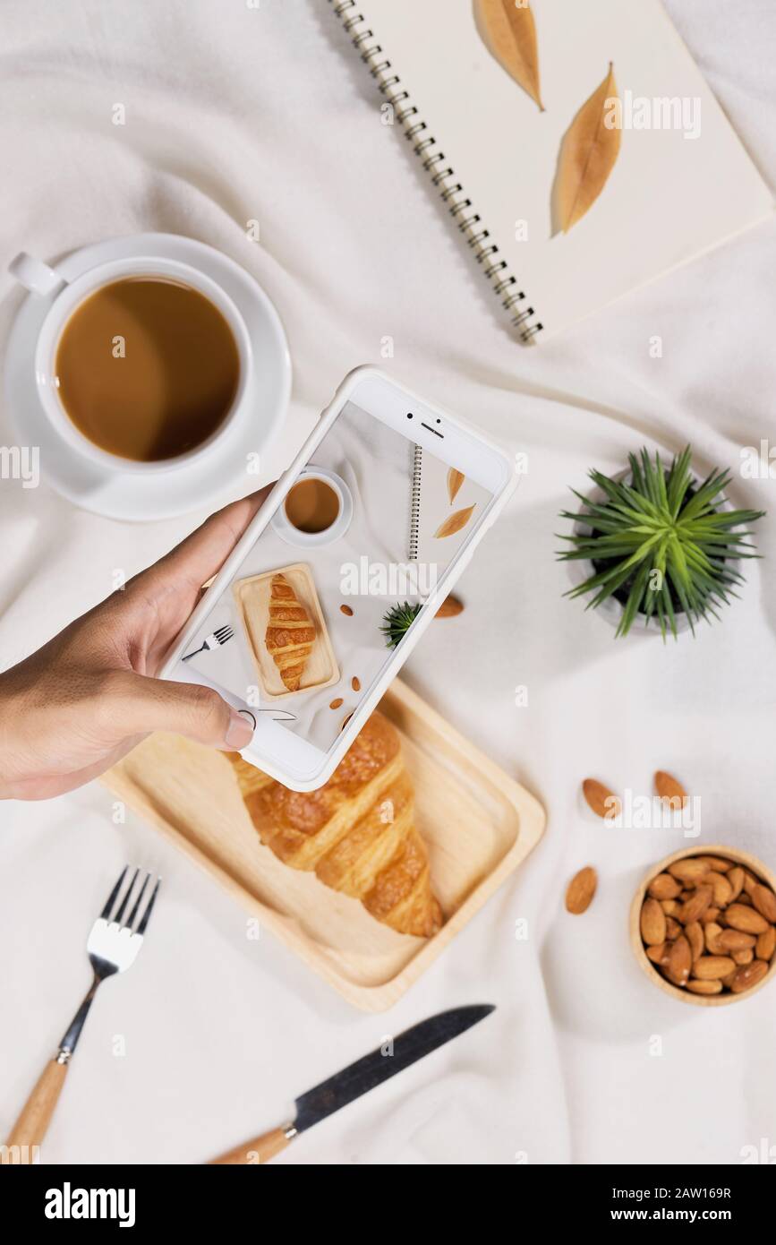 Caffè, croissant, piante, mandorle e taccuino su una scrivania bianca erano piatti Foto Stock