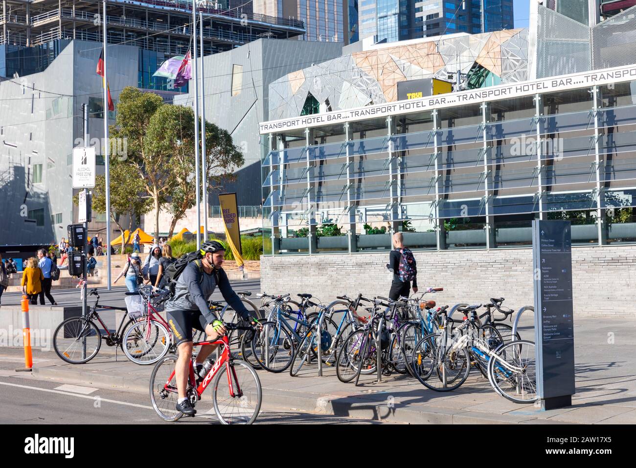 Uomo a cavallo della sua bicicletta passato biciclette immagazzinate nel centro di Melbourne, Victoria, Australia Foto Stock