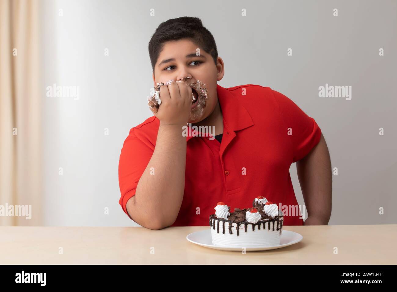 Ragazzo giovane che divorava la torta con le mani. (Obesità) Foto Stock