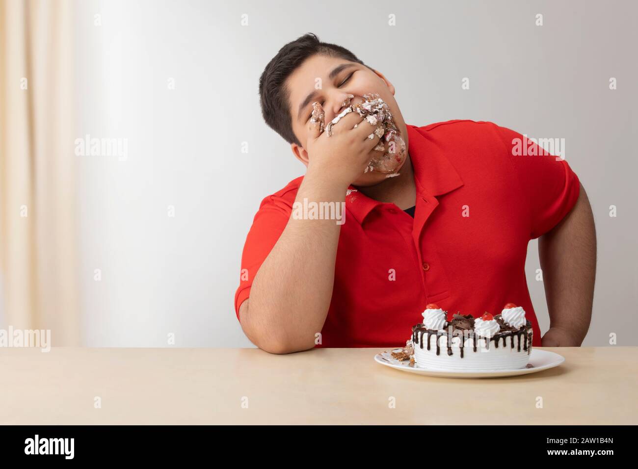 Ragazzo giovane che gli insaccava la bocca con la torta. (Obesità) Foto Stock