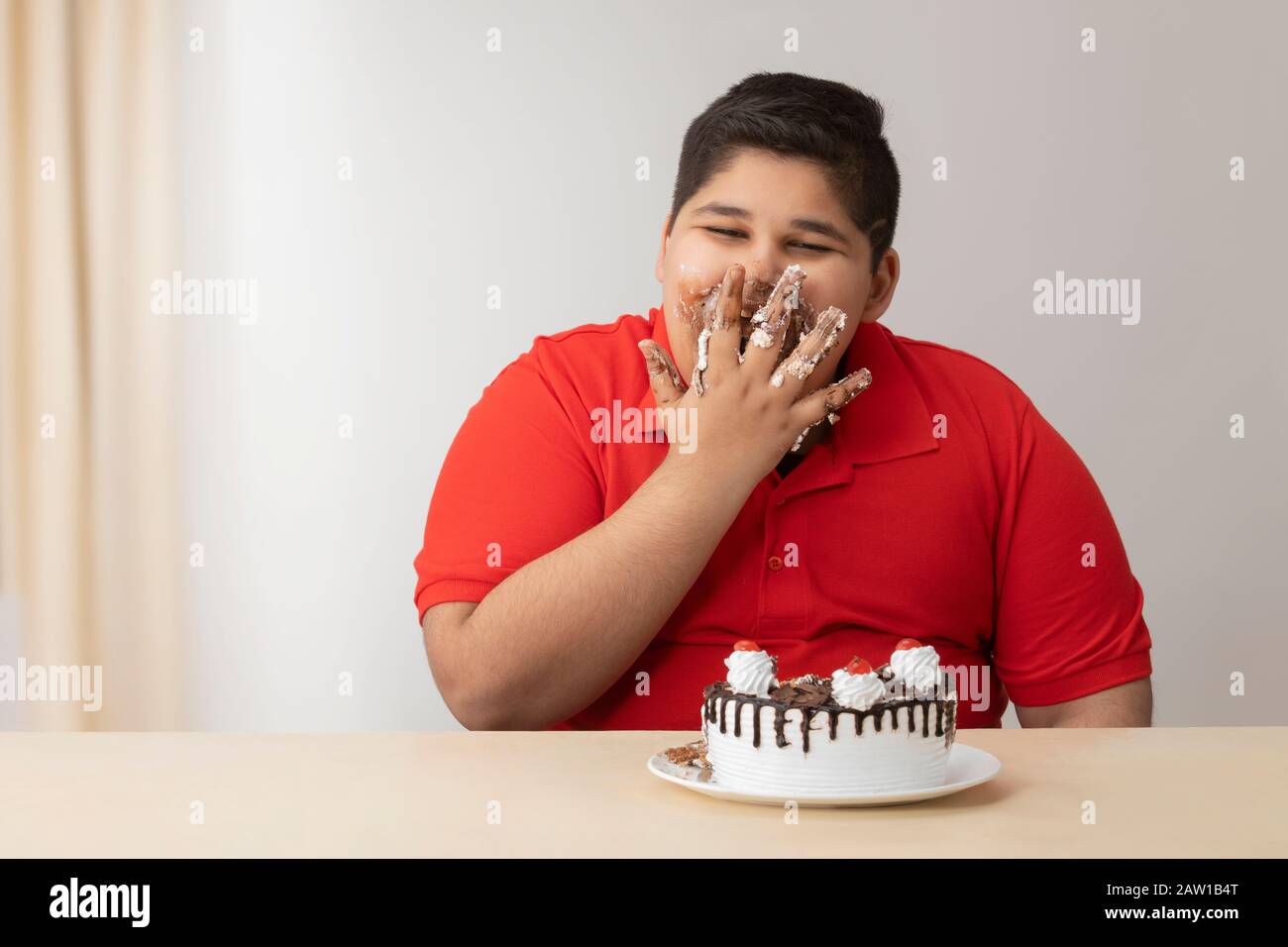 Ragazzo giovane che gli insaccava la bocca con la torta. (Obesità) Foto Stock