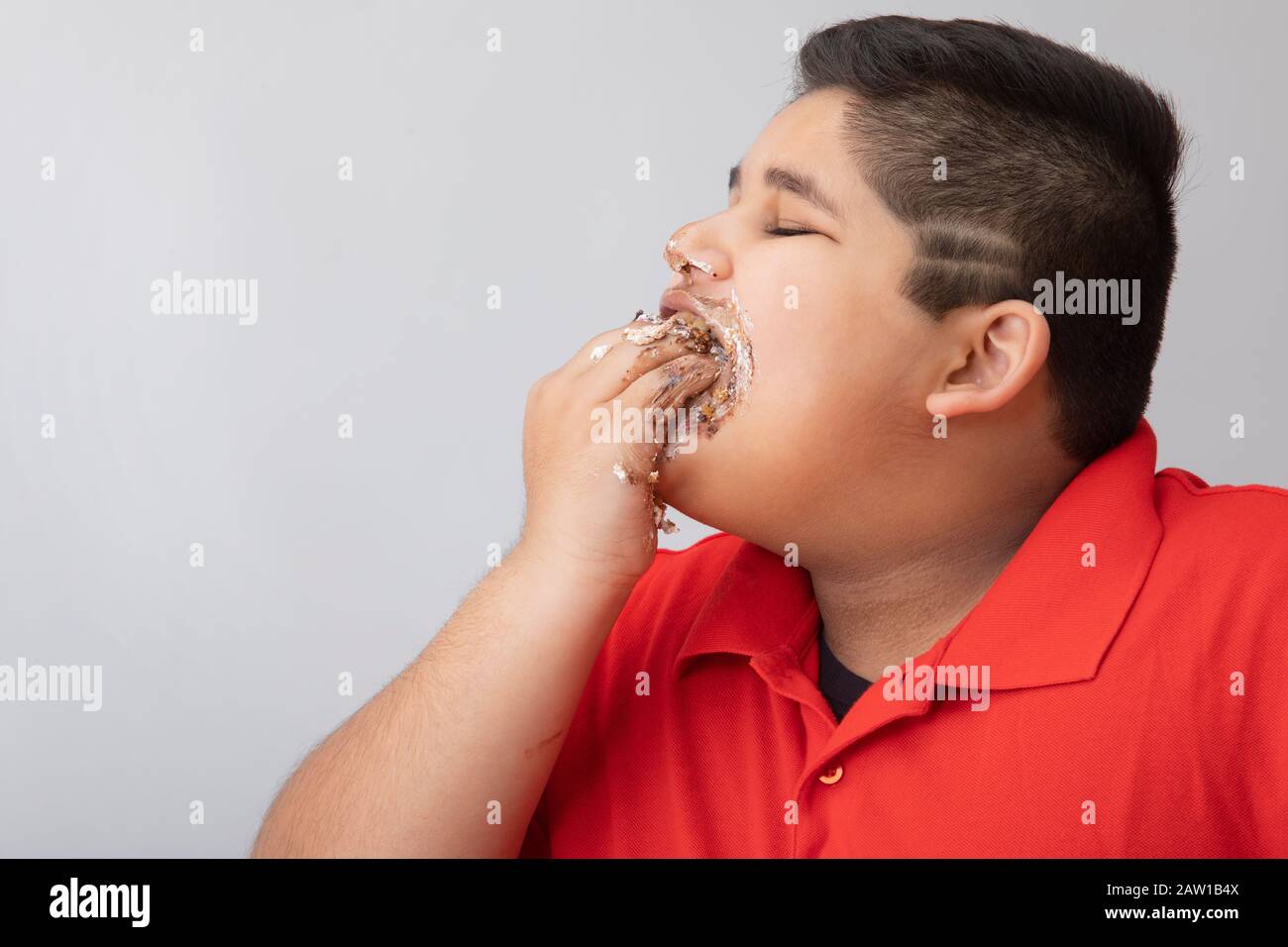Ragazzo giovane che leccava le mani coperto di torta. (Obesità) Foto Stock