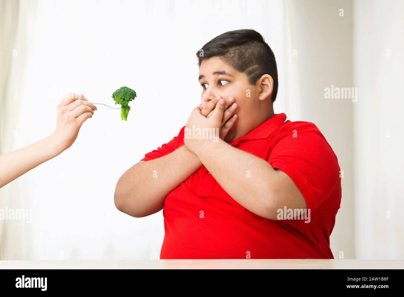 Ragazzo giovane che gli copriva la bocca lontano dai broccoli. (Obesità) Foto Stock