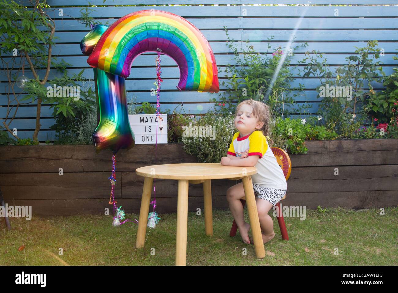 Ragazza di 3 anni seduta ad un tavolo che guarda la stufa in un giardino, Regno Unito Foto Stock