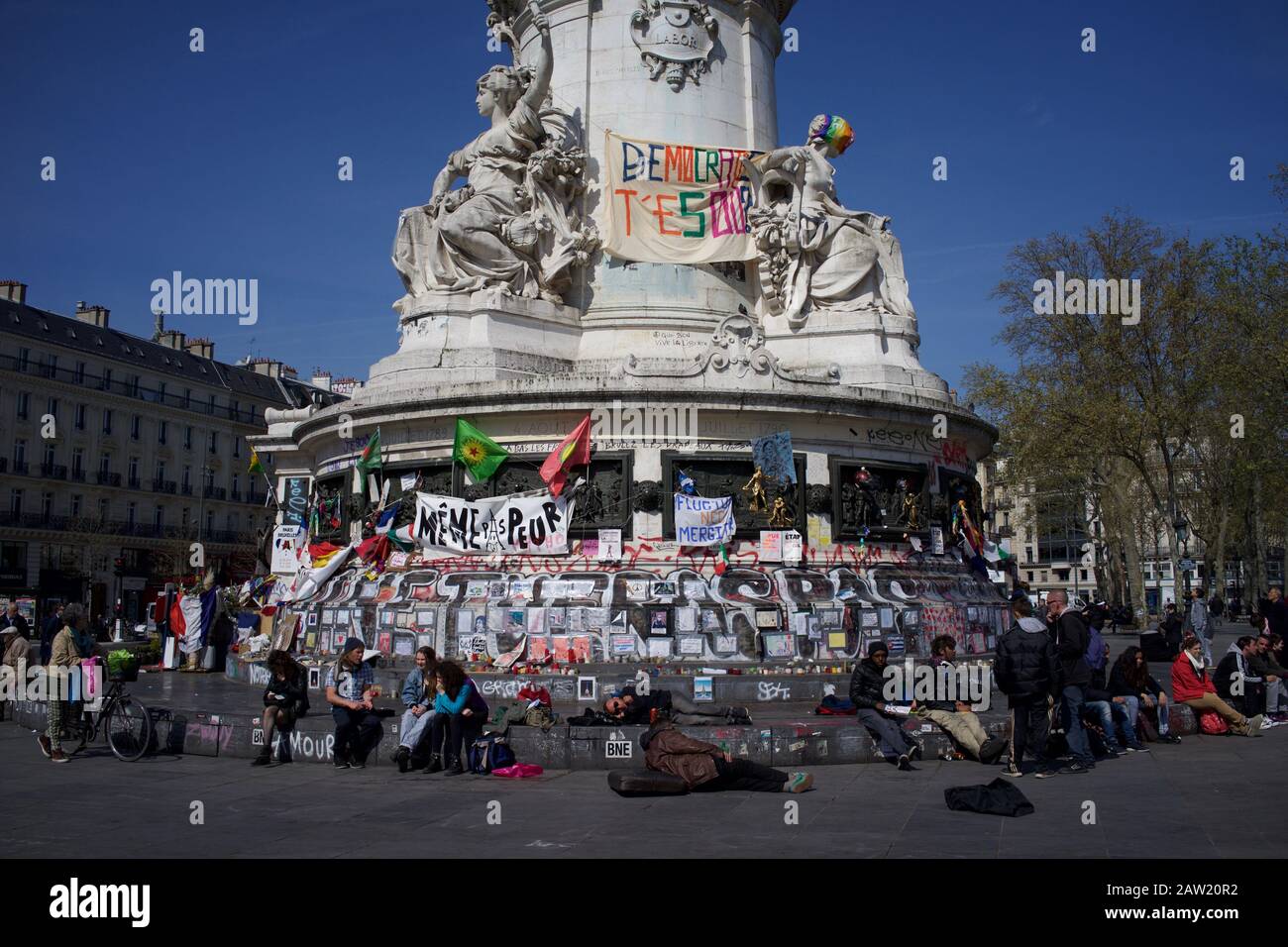 Persone sedute su gradini della statua di Marianne di fronte ai messaggi per ricordare le vittime degli attacchi di Parigi e Bruxelles, Place de la République, Parigi, Francia - aprile 2016 Foto Stock