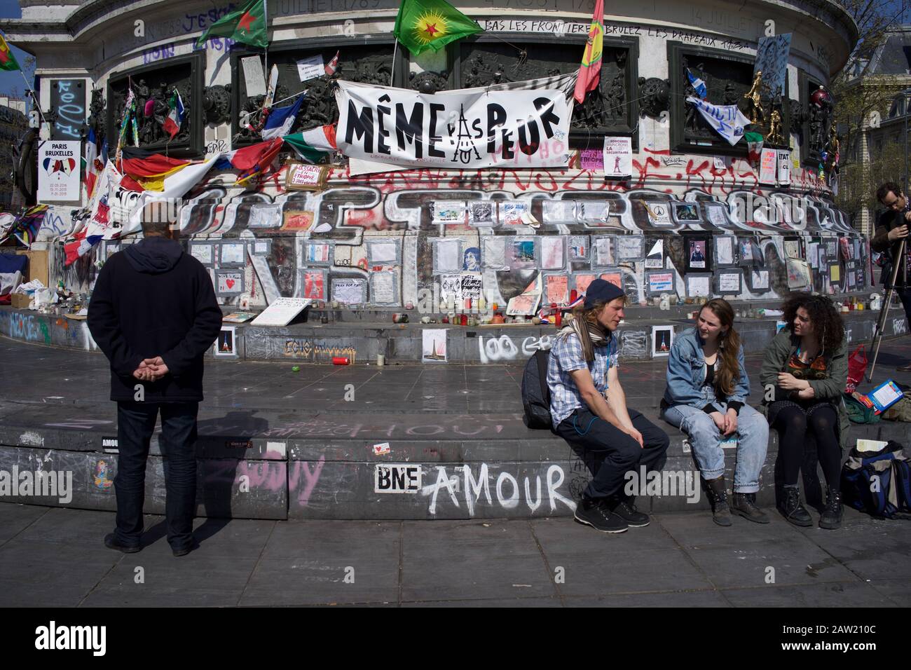 Persone sedute su gradini della statua di Marianne davanti a messaggi che commemorano le vittime degli attacchi di Parigi e Bruxelles, Place de la République, Parigi, Francia - aprile 2016 Foto Stock