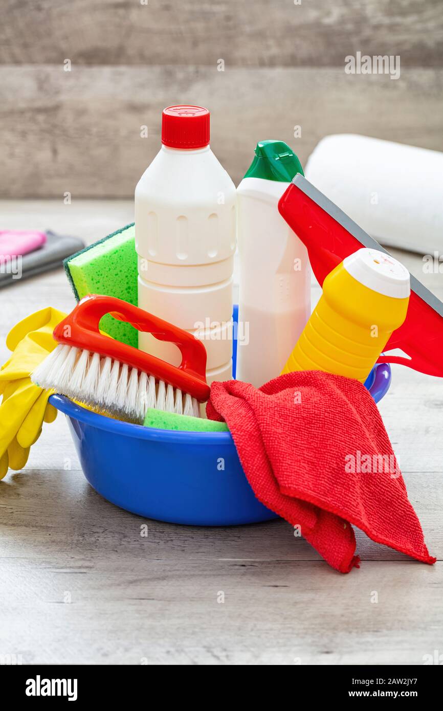 Prodotti per la pulizia sul pavimento, sfondo interno casa. Bottiglie di detergente chimico in un recipiente blu. Pulizia sanitaria domestica o aziendale Foto Stock