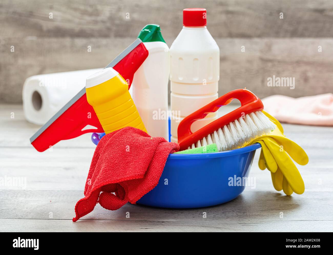 Prodotti per la pulizia sul pavimento, sfondo interno casa. Bottiglie di detergente chimico in un recipiente blu. Pulizia sanitaria domestica o aziendale Foto Stock
