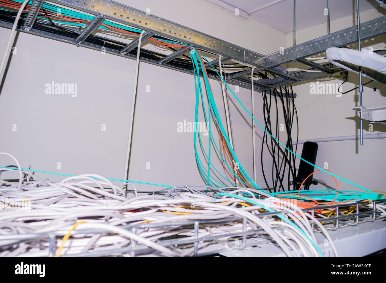 I cavi disordinati vengono aggrovigliati tra loro sul soffitto sospeso del data center della sala server. Cavi Internet in fibra ottica e fili elettrici si trovano Foto Stock