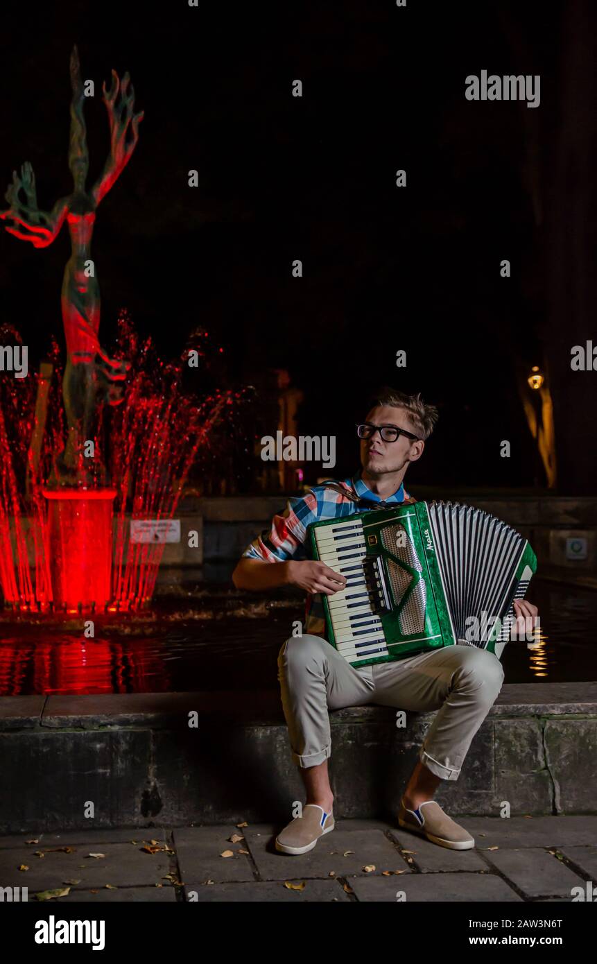 Kaunas, Lituania - 19 05 2013: Giovane musicista di talento inidentificato che suona la fisarmonica nel vicolo della libertà in fontana illuminata e sculpt della dea del mare Foto Stock