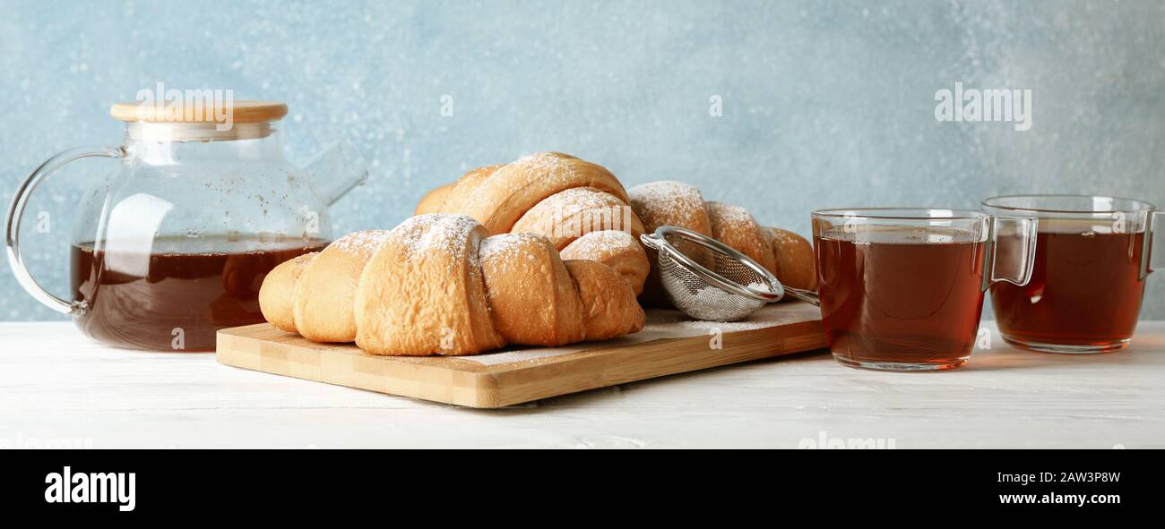 Gustosi croissant e tazze con tè su sfondo di legno, spazio per il testo Foto Stock