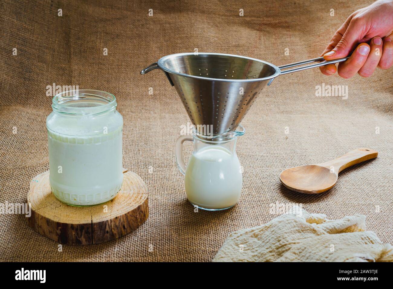 Mano d'uomo versa il latte il kefir in una caraffa per preparare una colazione sana per il microbiota intestinale. Foto Stock