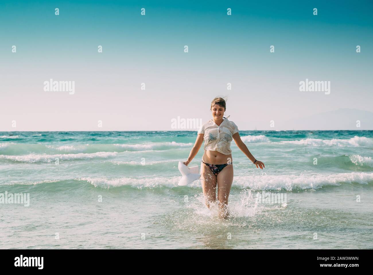 Giovane Donna Caucasica In Costume Da Bagno E Cappello Estivo A Piedi In Acqua Di Mare. Vacanza Su Sea Ocean Beach. Foto Stock