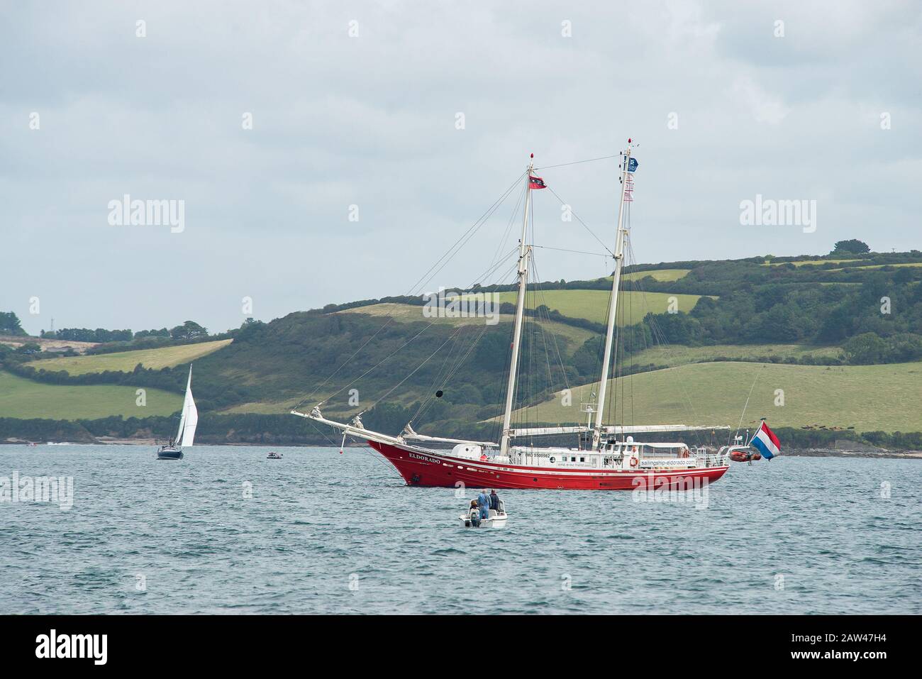 Elegante imbarcazione a vela con doppio scafo rosso ancorata alla Fal pronta per l'evento Tall Ships. Avvicinati da una dingy del motore. Foto Stock