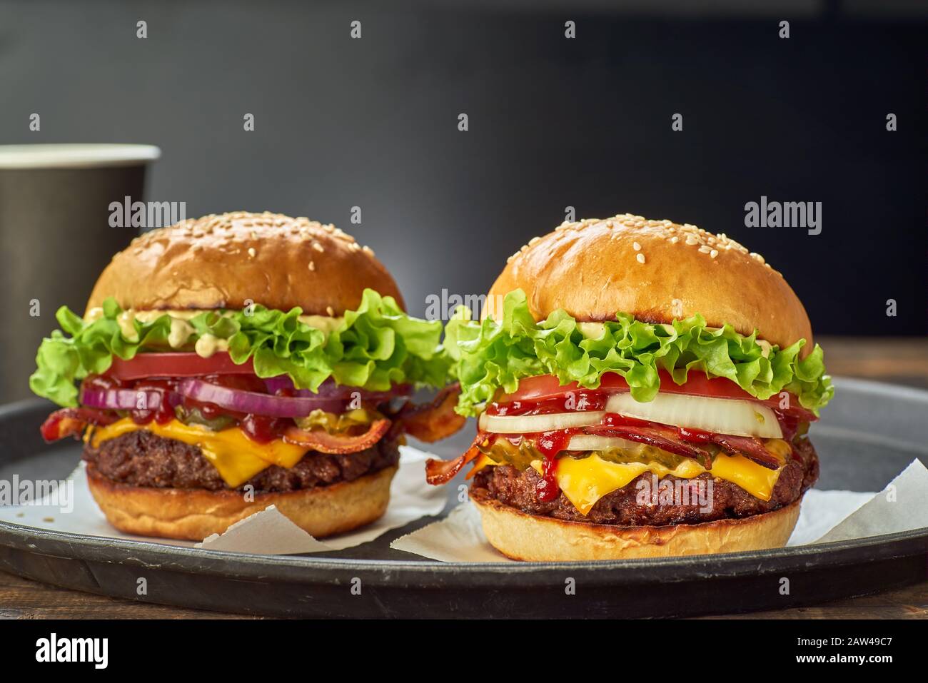 Due hamburger e una tazza di bevanda di carta serviti su sfondo scuro Foto Stock
