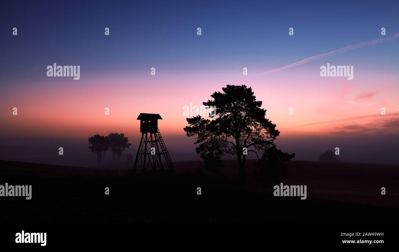 Paesaggio rurale con silhouette di osservazione o torre di caccia su un campo all'alba. Foto Stock