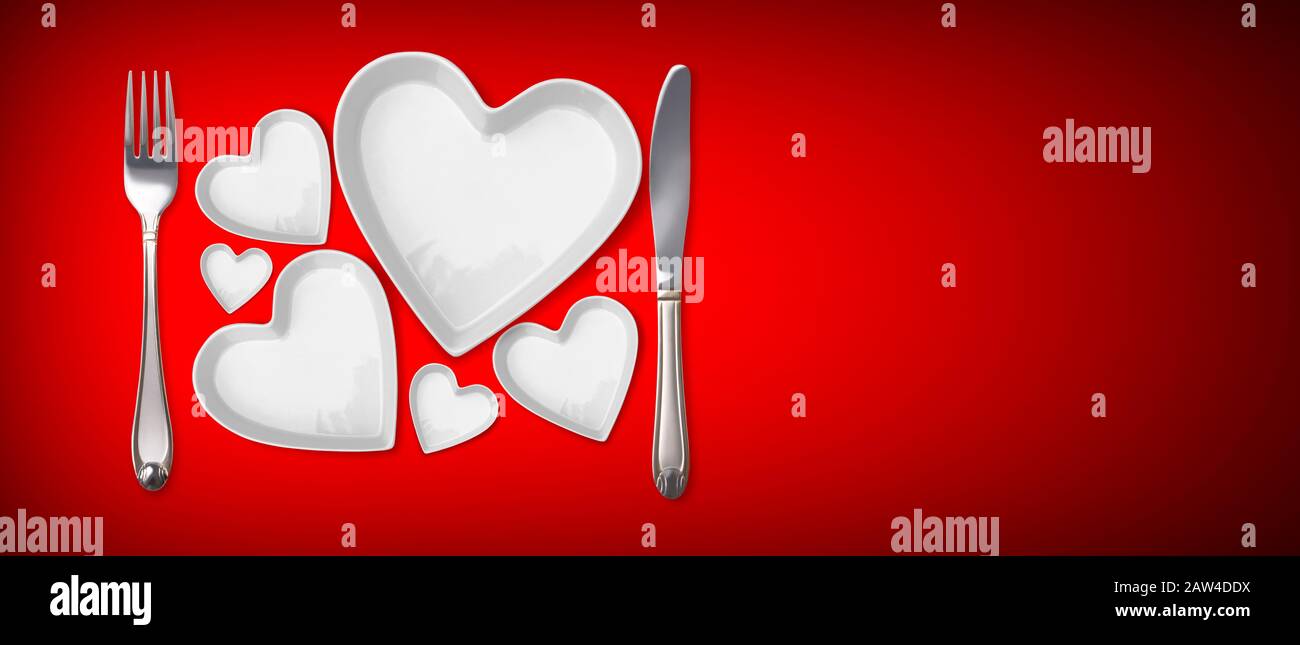 Appuntamenti da tavolo con piastre a forma di cuore modello con piastre vuote, forcella, coltello su sfondo rosso Foto Stock