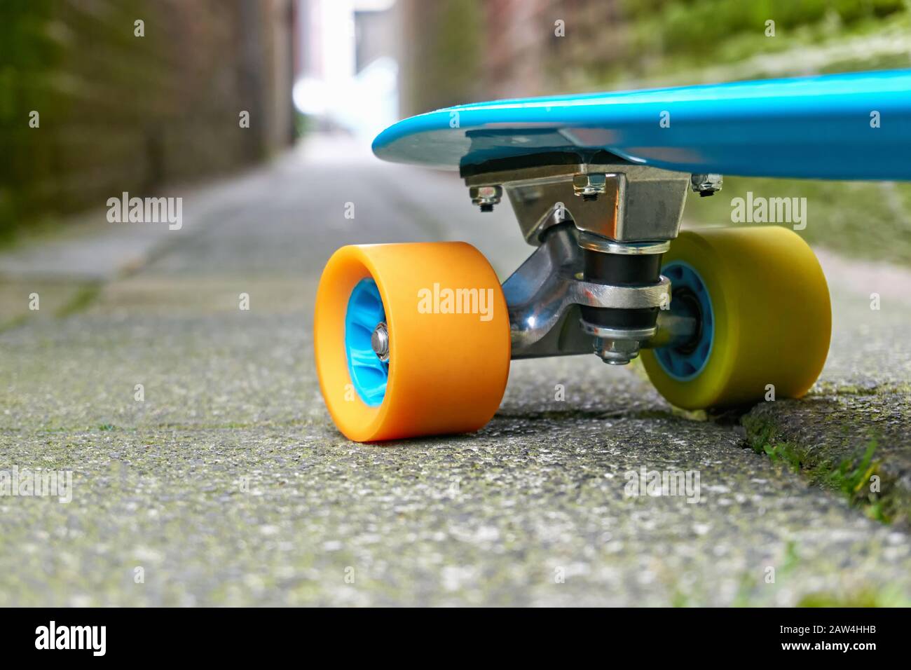 Fronte di mini Cruiser in plastica blu penny board o skate board con ruote  gialle e arancioni su piastrelle di cemento in un vicolo con luce alla fine  Foto stock - Alamy