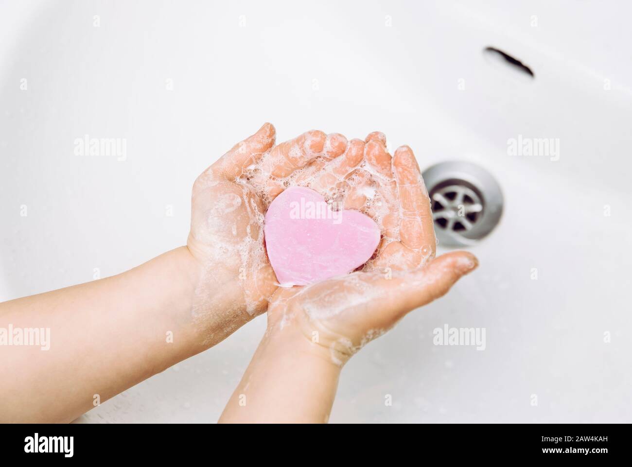 Importanza dell'igiene personale. Vista piatta della disposizione del bambino lavando le mani sporche con la barra del sapone della forma del cuore rosa, molta schiuma. Spazio di copia. Foto Stock