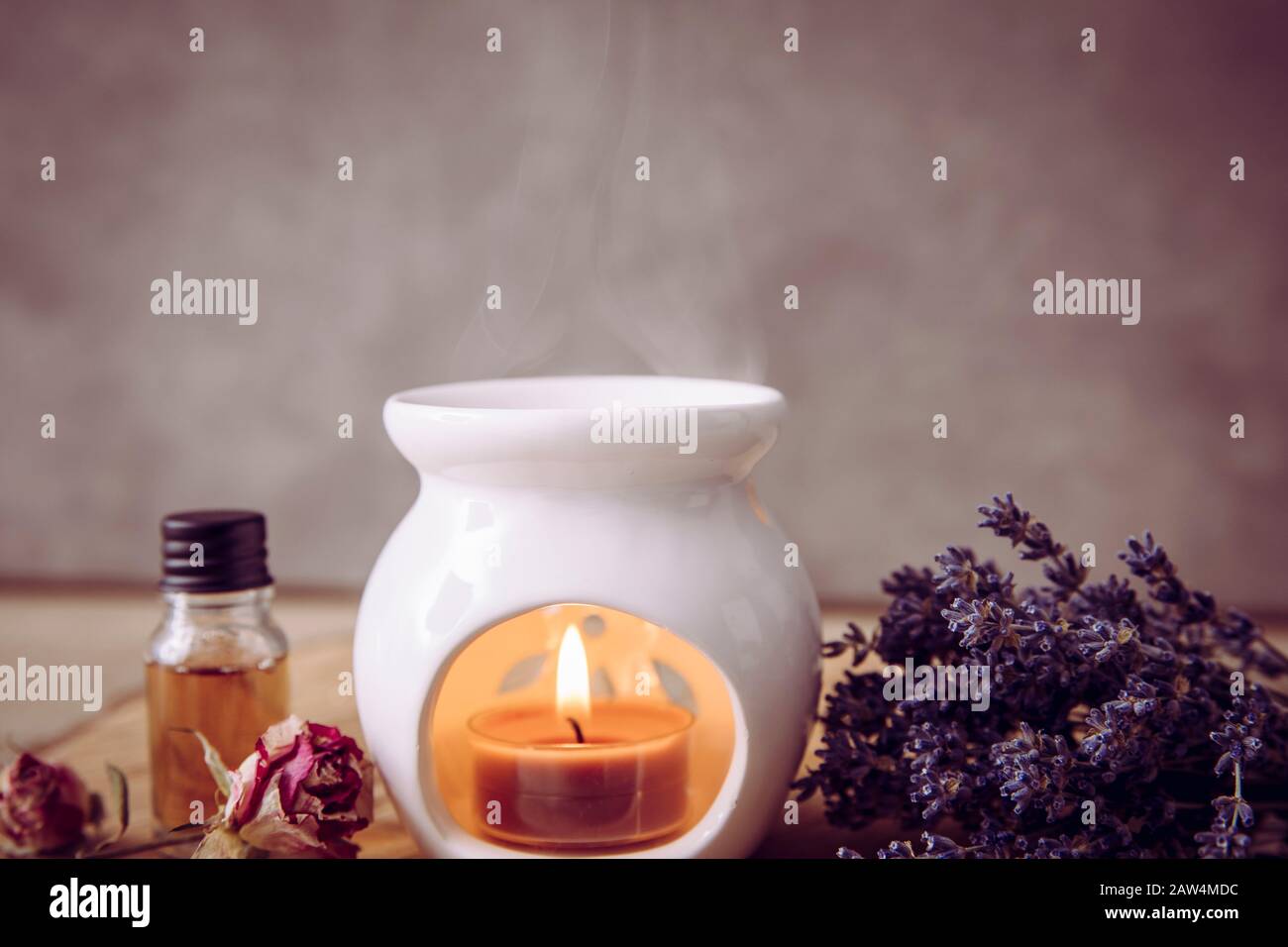 Immagine in stile vintage di candela bianca in ceramica aroma lampada ad olio con bottiglia d'olio essenziale e petali di fiori secchi su disco di legno di pino naturale, fondo secco Foto Stock