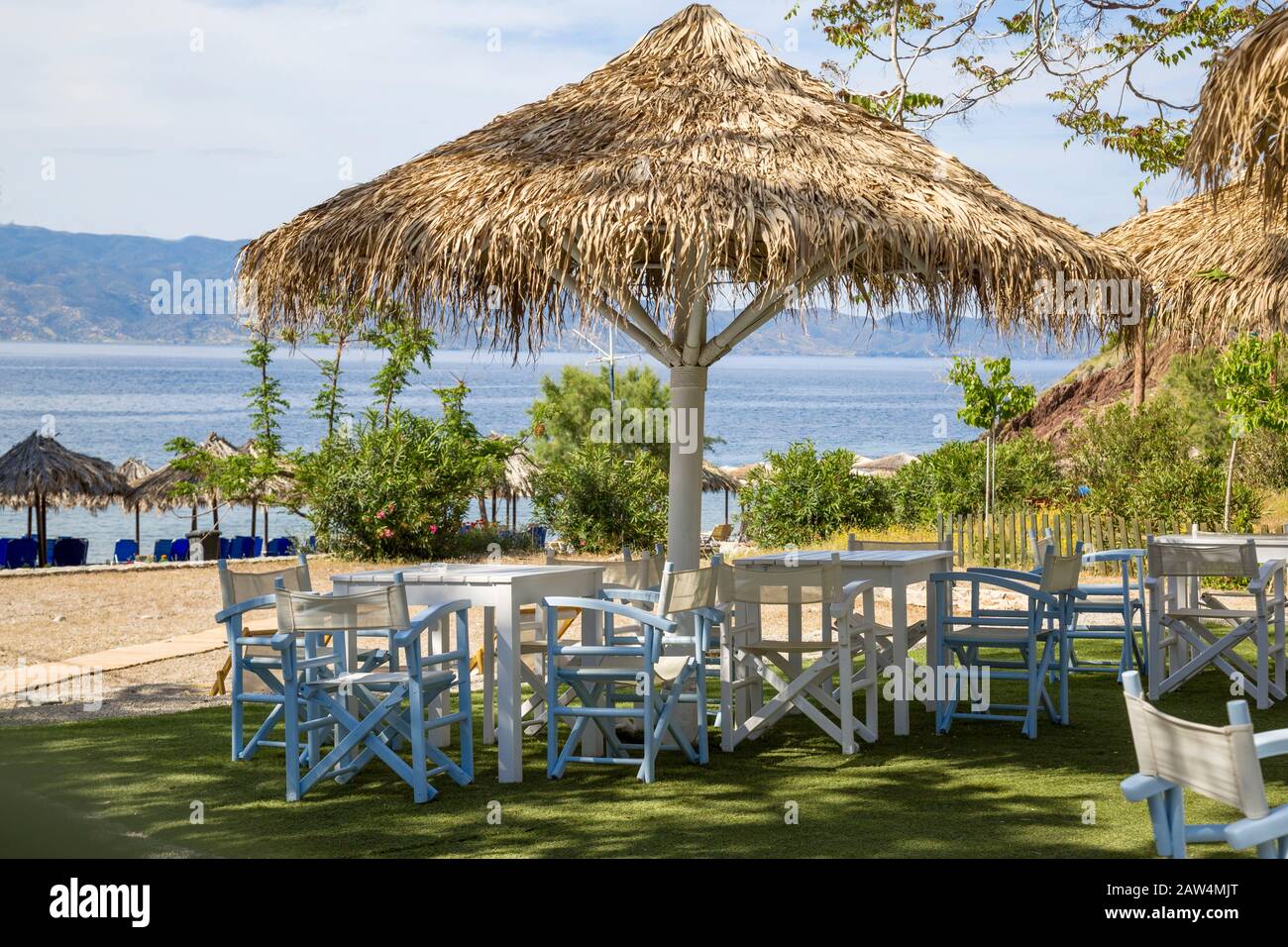 Palapa ombreggiava tavoli e sedie sulla spiaggia di Vlichos sull'isola di Hydra, una delle isole Saroniche nel Mar Egeo. Foto Stock