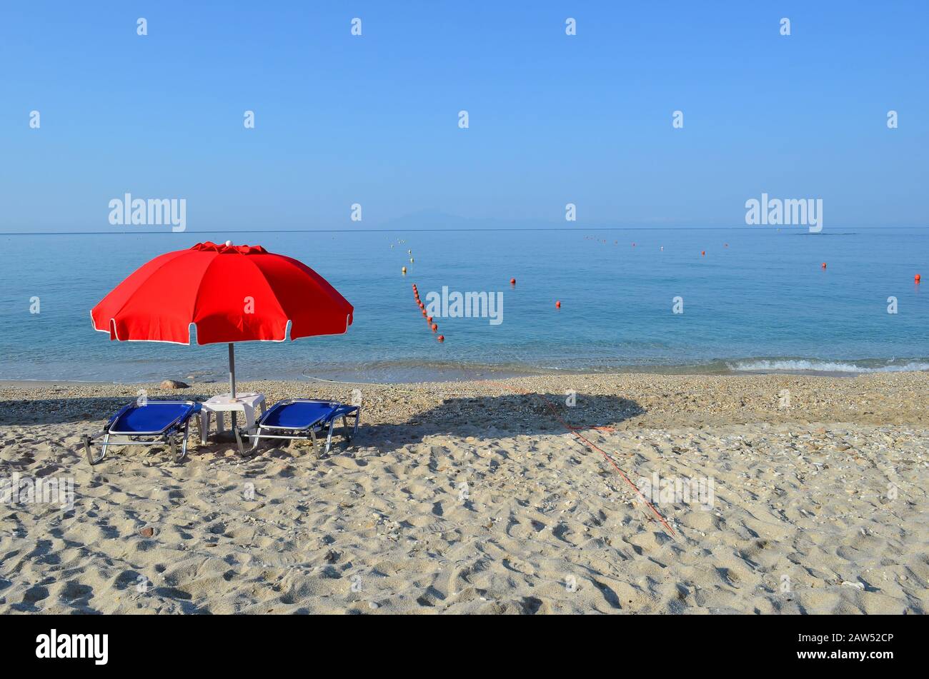 Ombrellone rosso e due sdraio sulla spiaggia di sabbia vuota Foto Stock