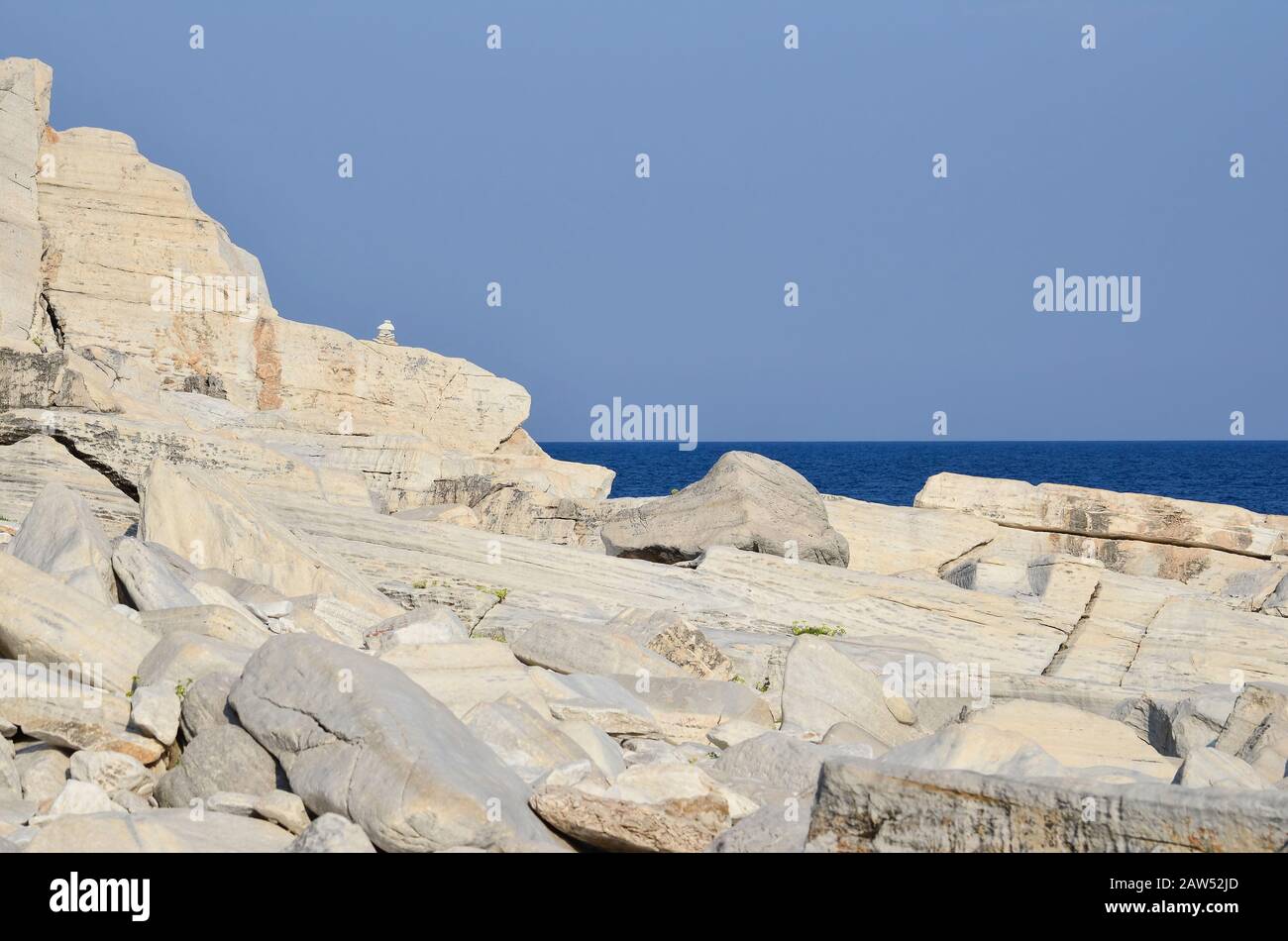 Scogliera di marmo, mare, cielo azzurro chiaro e piccole pile di pietre zen di marmo su roccia di marmo solido Foto Stock
