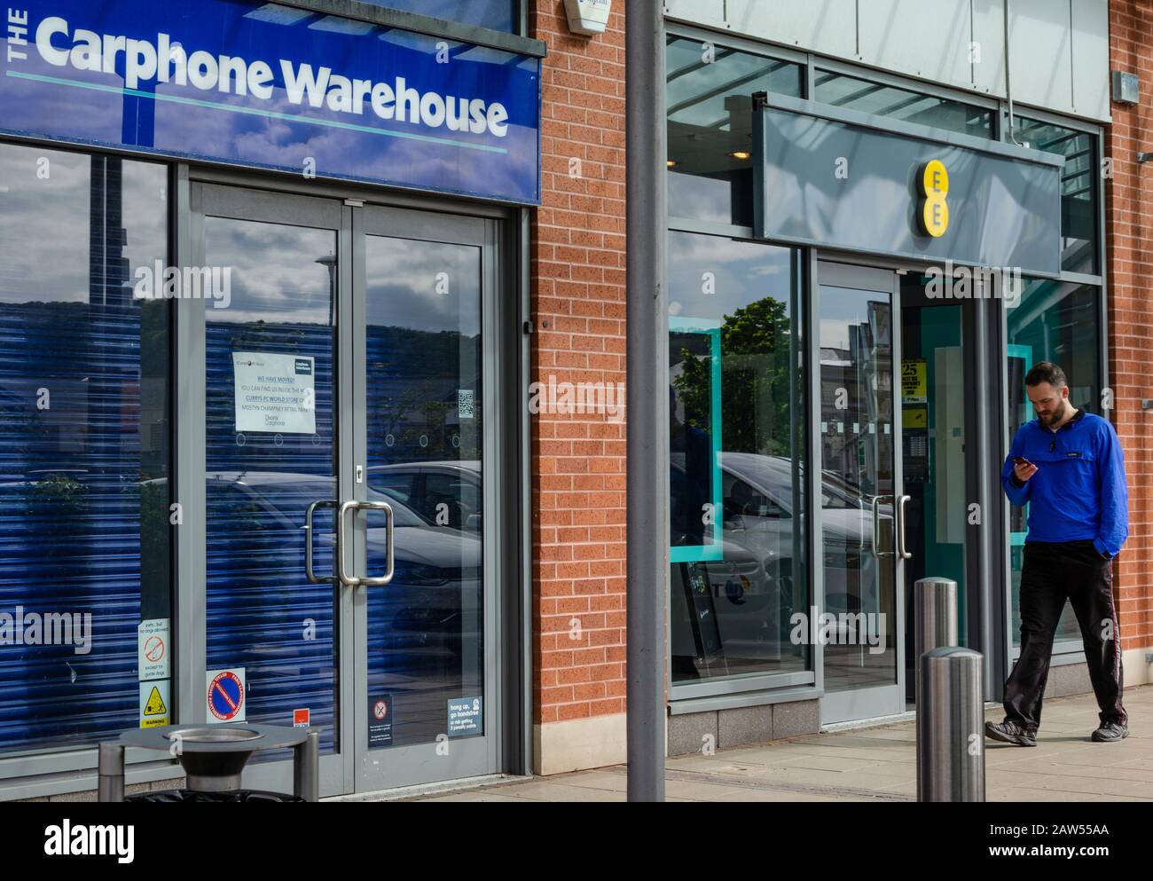Llanddudno, Regno Unito: 06 maggio 2019: Un uomo controlla il suo telefono cellulare mentre cammina oltre un negozio di telefonia mobile EE aperto. Accanto c'è un ramo del Carphone W. Foto Stock
