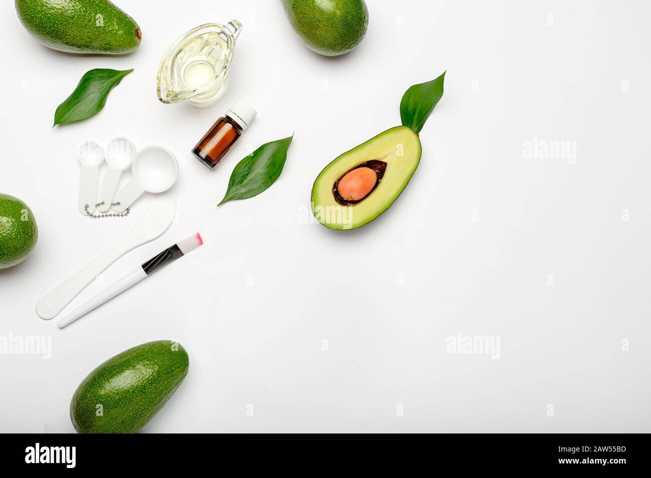 Set di cosmetologia per la cottura, applicazione maschera facciale. Avocado, foglie, spatola, pennello, cucchiai di misura, olio essenziale, olio su fondo bianco con copia Foto Stock
