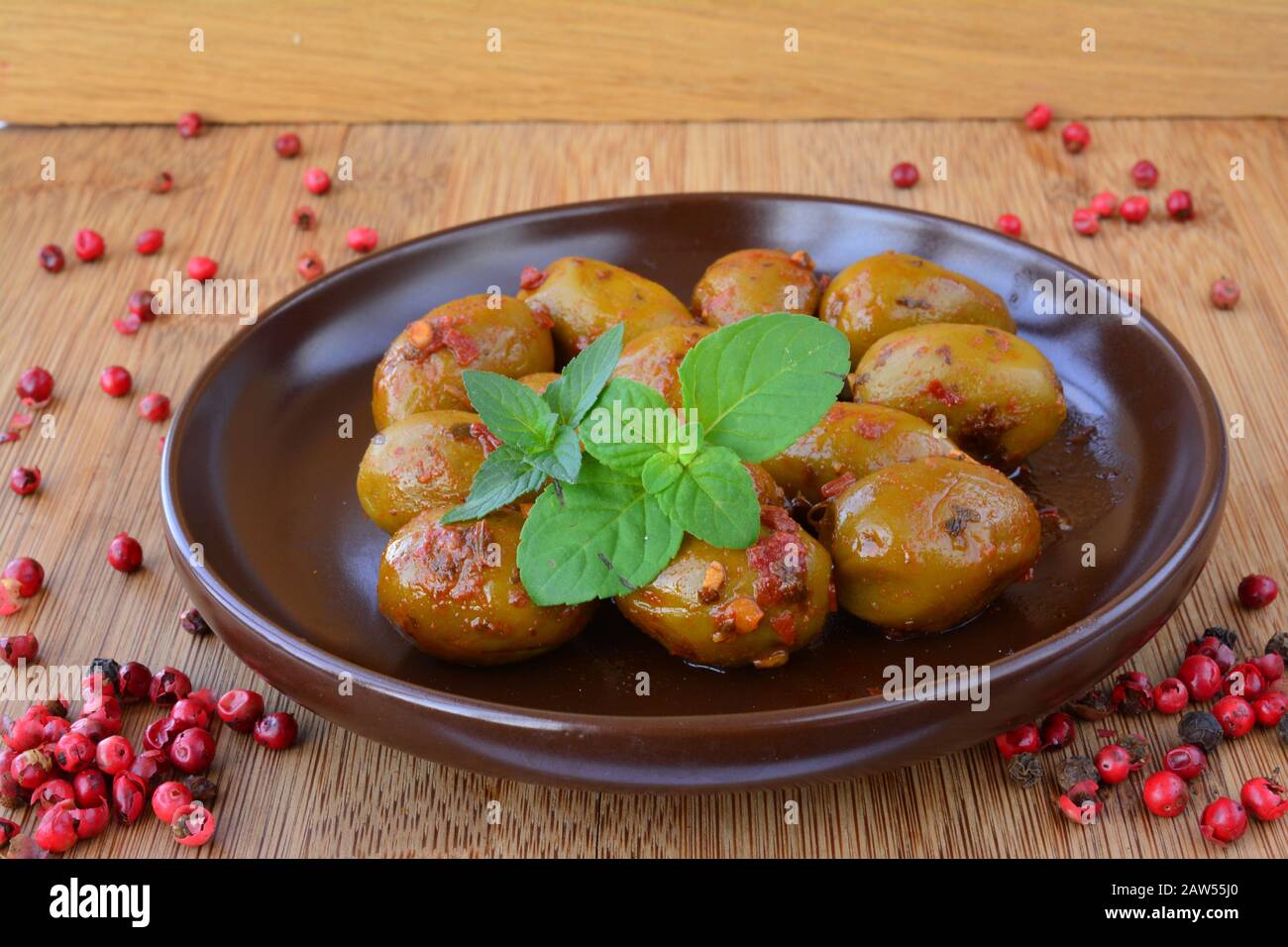 Olive verdi pepite in piattino di ceramica marrone, calde e piccanti, decorate con foglie di menta verde e pepe rosso su sfondo di legno Foto Stock