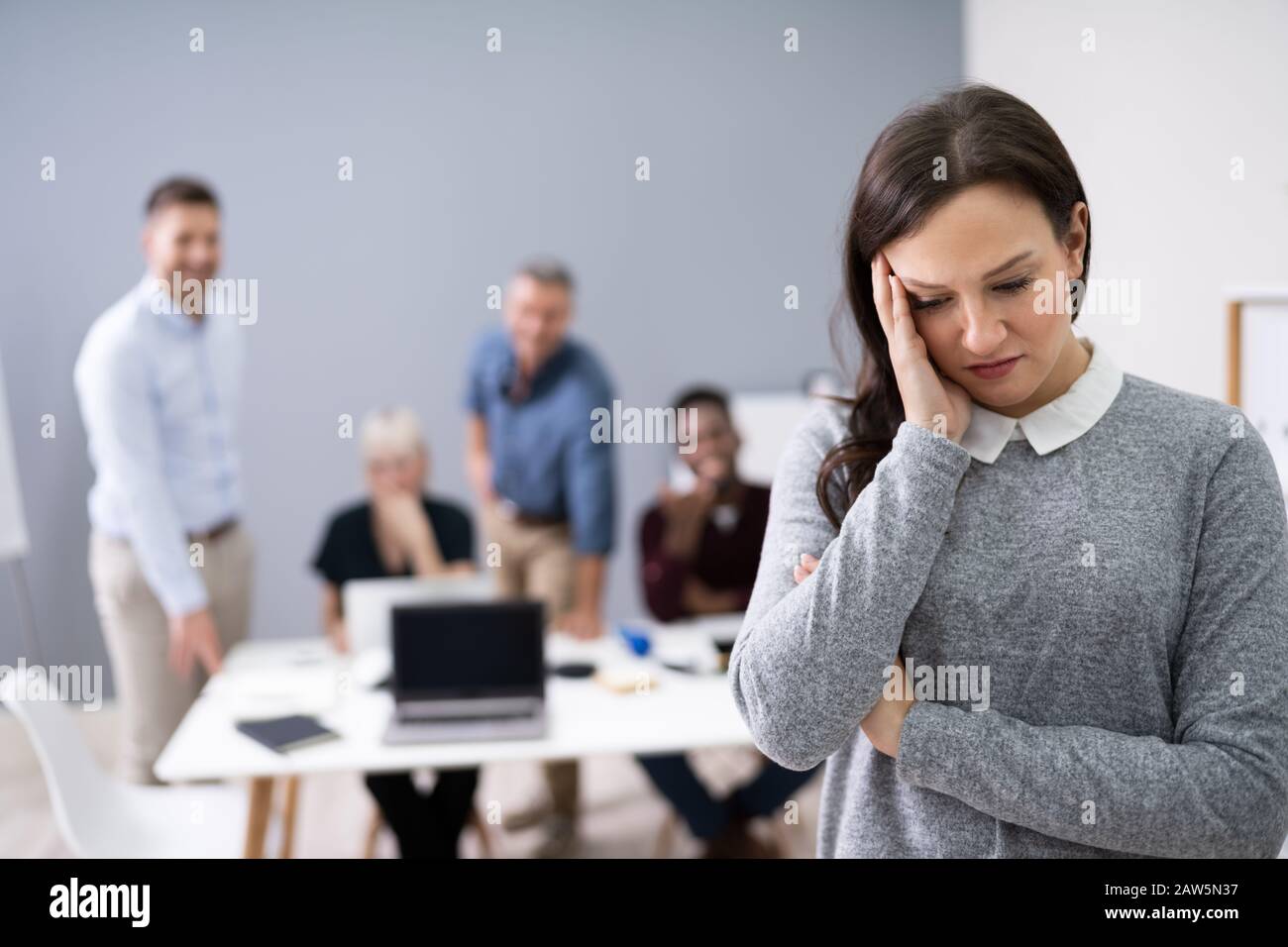 Ritratto di un triste imprenditrice con colleghi ridere su di lei in background Foto Stock