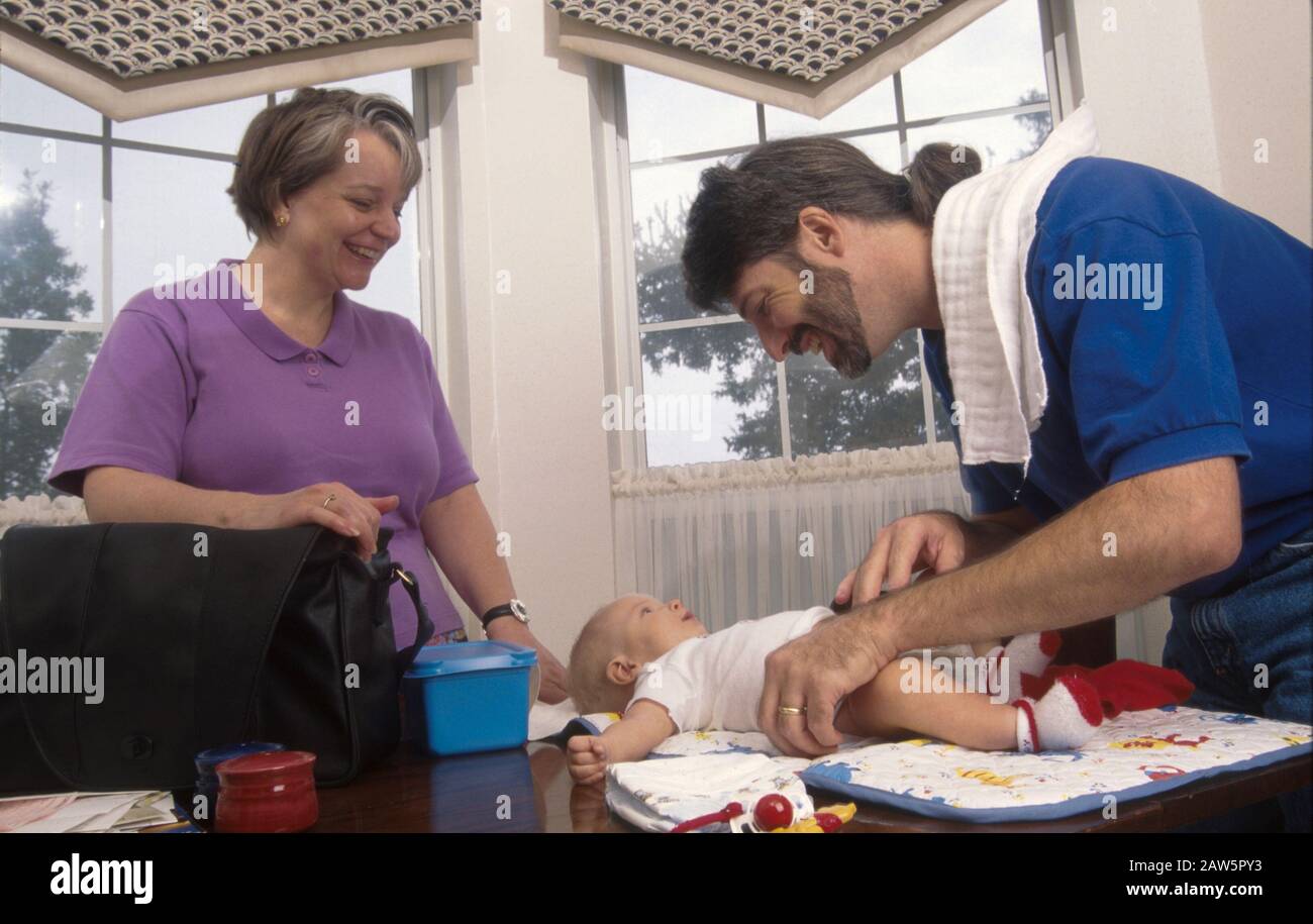 Il papà di soggiorno a casa cambia il pannolino di tre mesi mentre la moglie guarda. Foto Stock