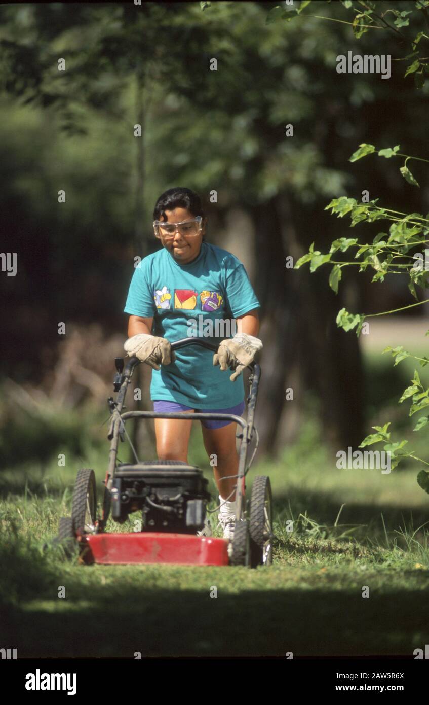 11-anno-ragazza ispanica falciando prato utilizzando le attrezzature di sicurezza in Austin Texas. Foto Stock