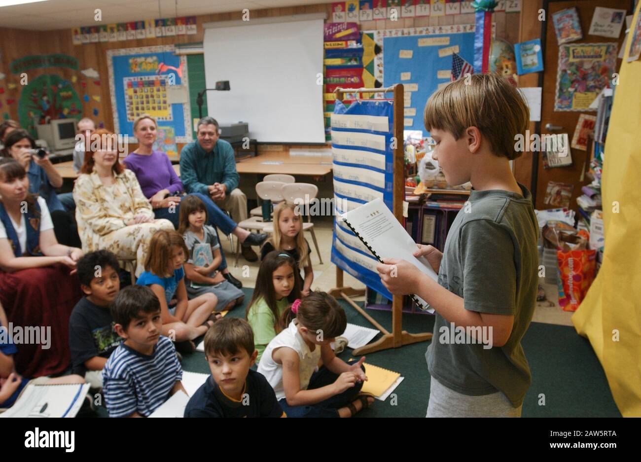 Studente di seconda classe alla Barton Hills Elementary School di Austin, Texas, legge il suo rapporto scientifico ai compagni di classe durante un 'gruppo editoriale' per i soggetti scientifici, mentre i genitori ascoltano nella parte posteriore della camera. Foto Stock